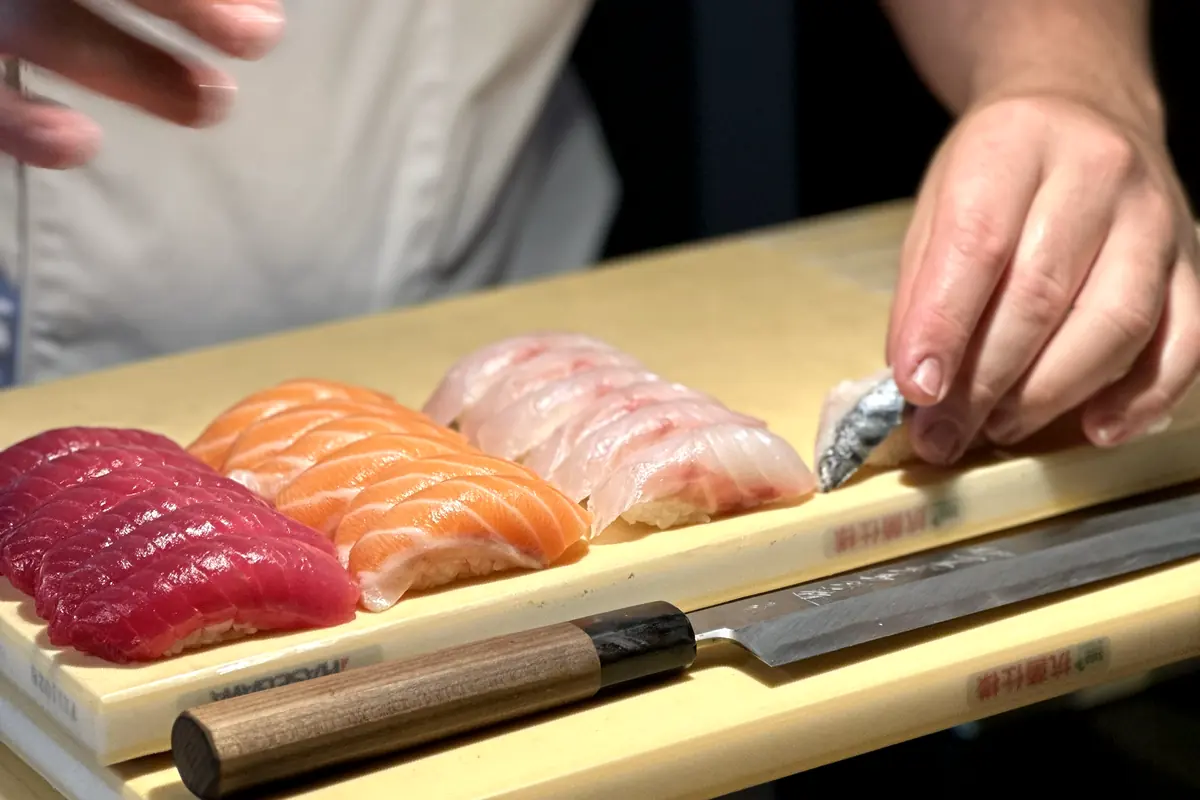 Les mains du chef posent un nigiri à côté d'un yanagiba sur la planche