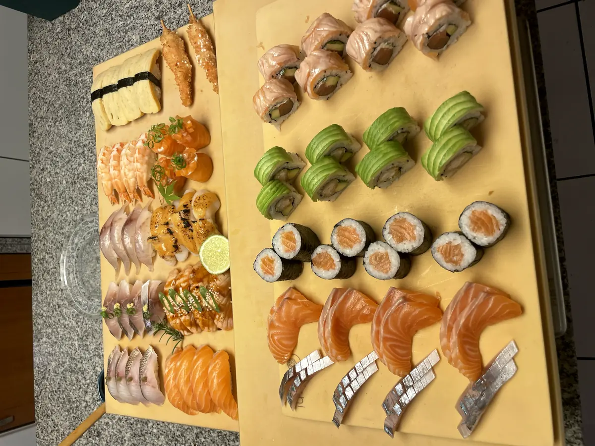 Deux planches de préparation : sashimis de saumon, makis et california rolls alignés