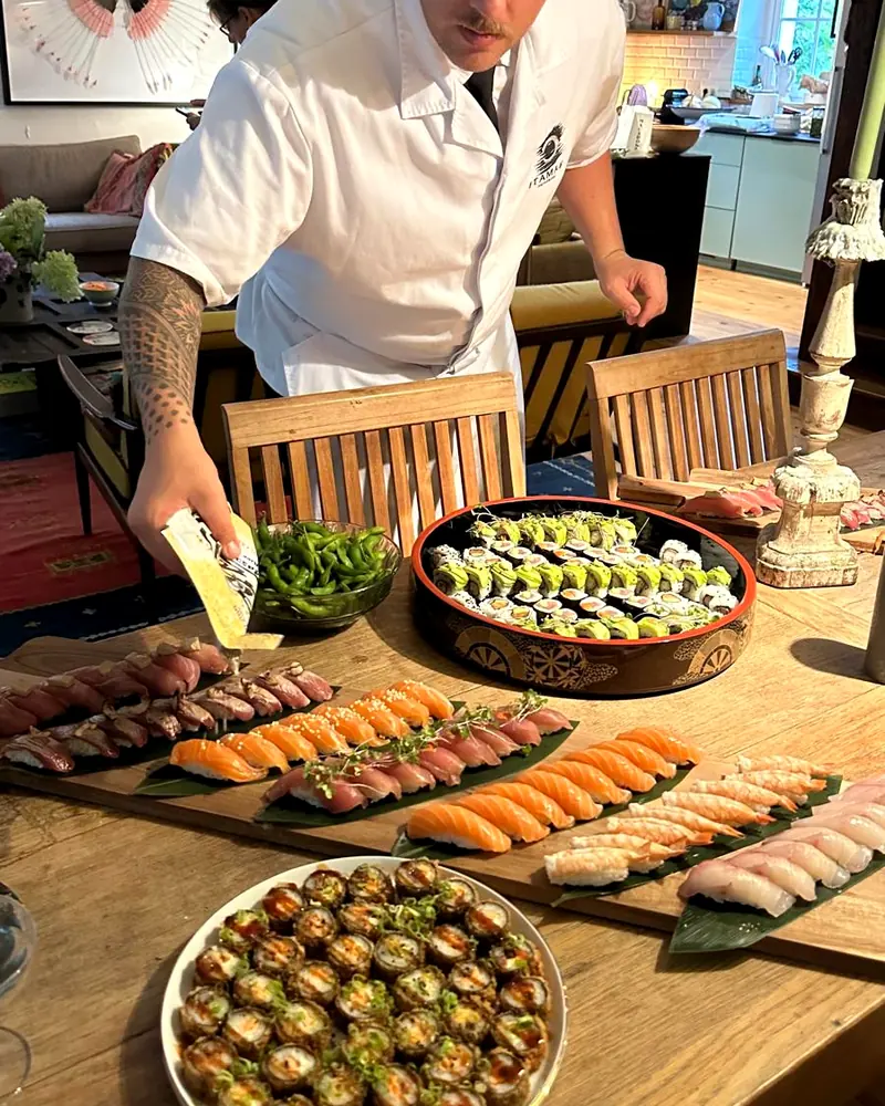 Le chef dresse une grande table de sushis chez un particulier, bougies allumées